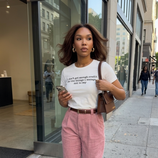 Woman walking on a city street holding a phone, wearing a white t-shirt and pink pants.