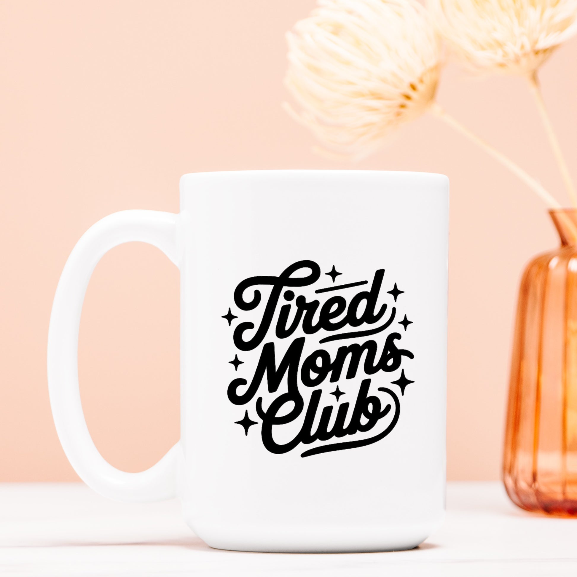 White mug with 'Tired Moms Club' text on a light pink background